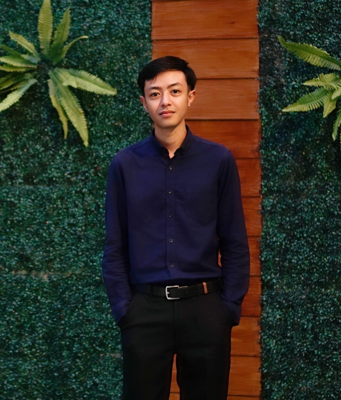 Formal portrait of Vincent Arjuna standing against a warm wooden panel